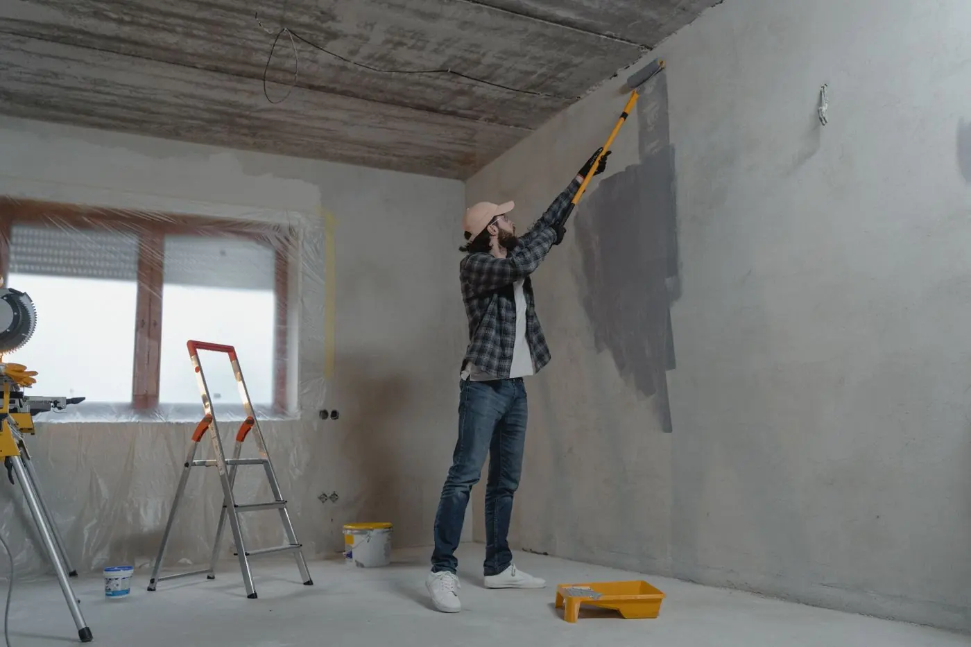 Vakman rolt een grijze muur in een kale ruimte met trap en raam
